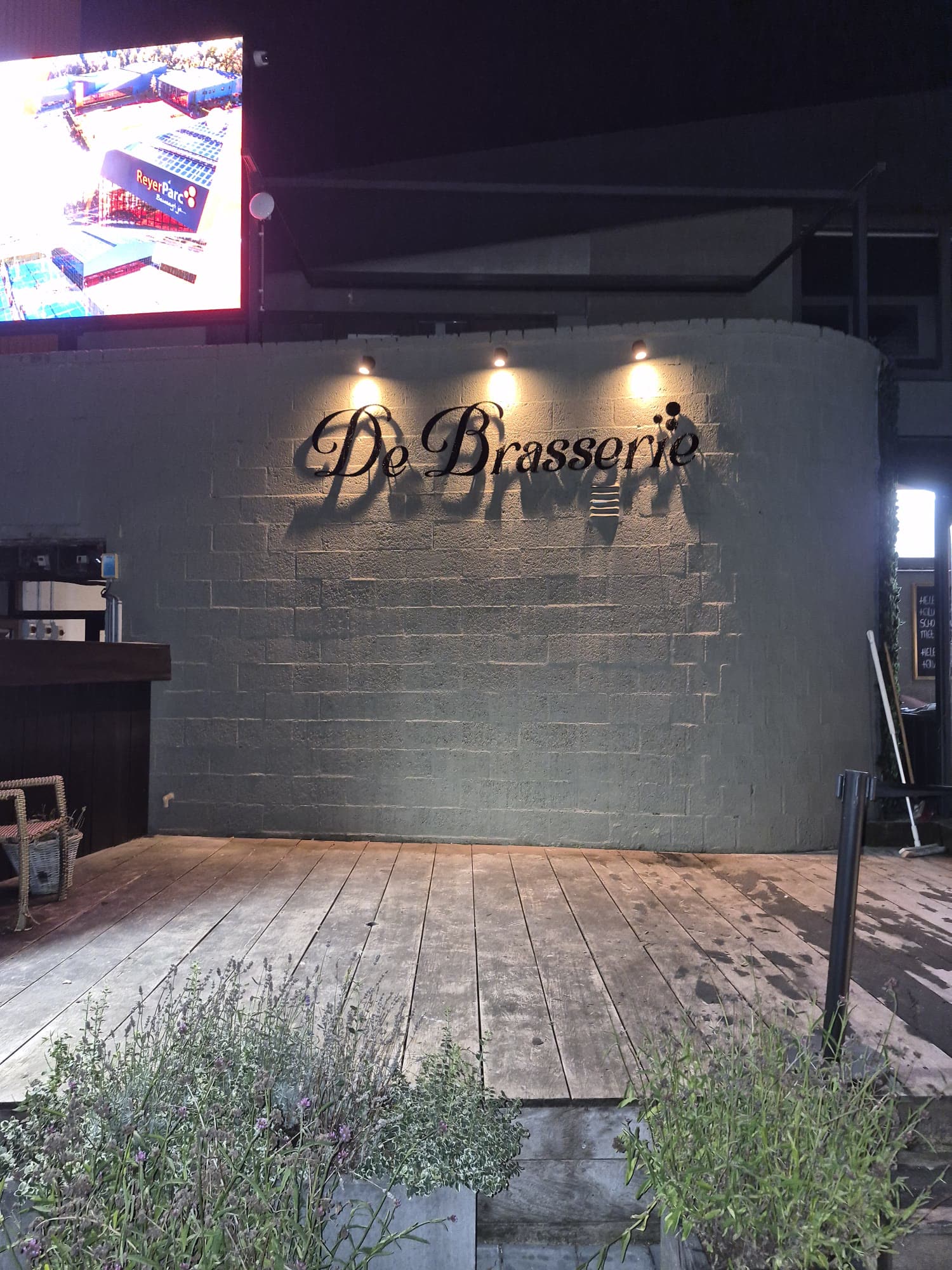 De gevelmuur van De Brasserie met aangelichte letters gezien vanaf het terras