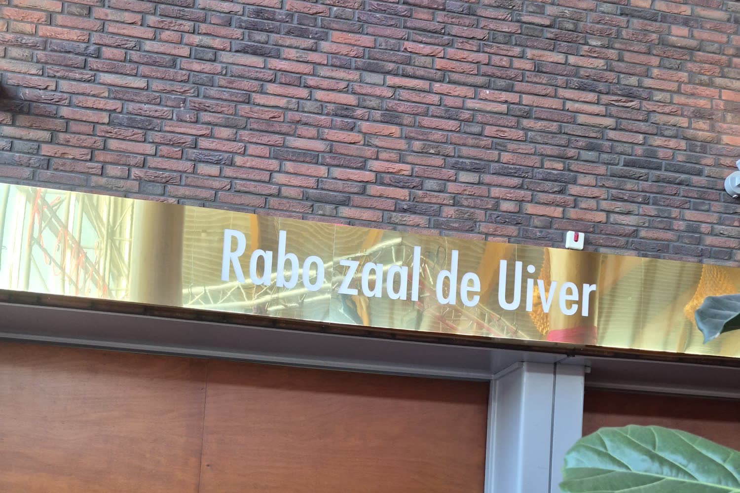 Gevelbord van Rabo zaal de Uiver in geborsteld goud op een bakstenen gevel