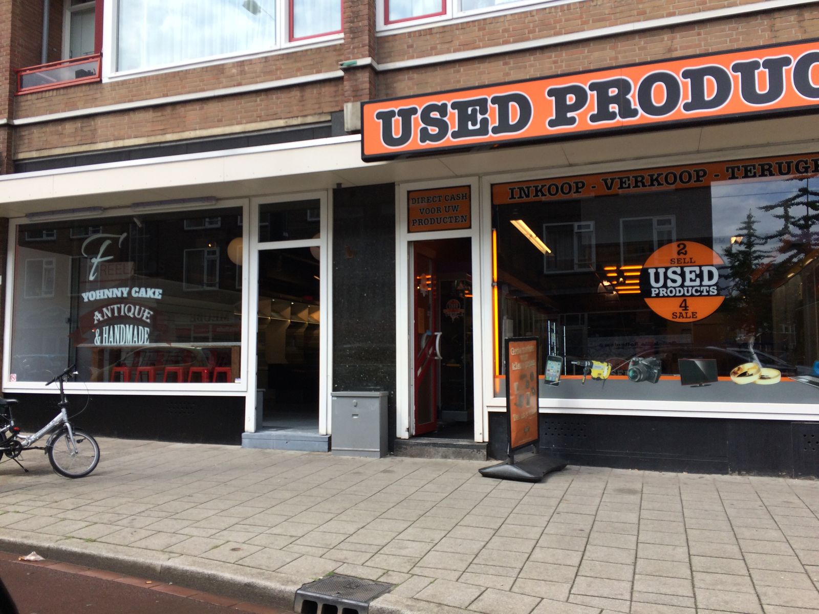 Yohnny Cake en buurpand Used Products — twee etalages met raambelettering naast elkaar in Rotterdamse winkelstraat